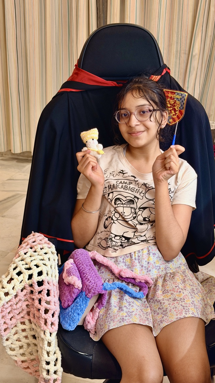 Avelyn holding a crochet doll and crochet hook, surrounded by her crochet projects